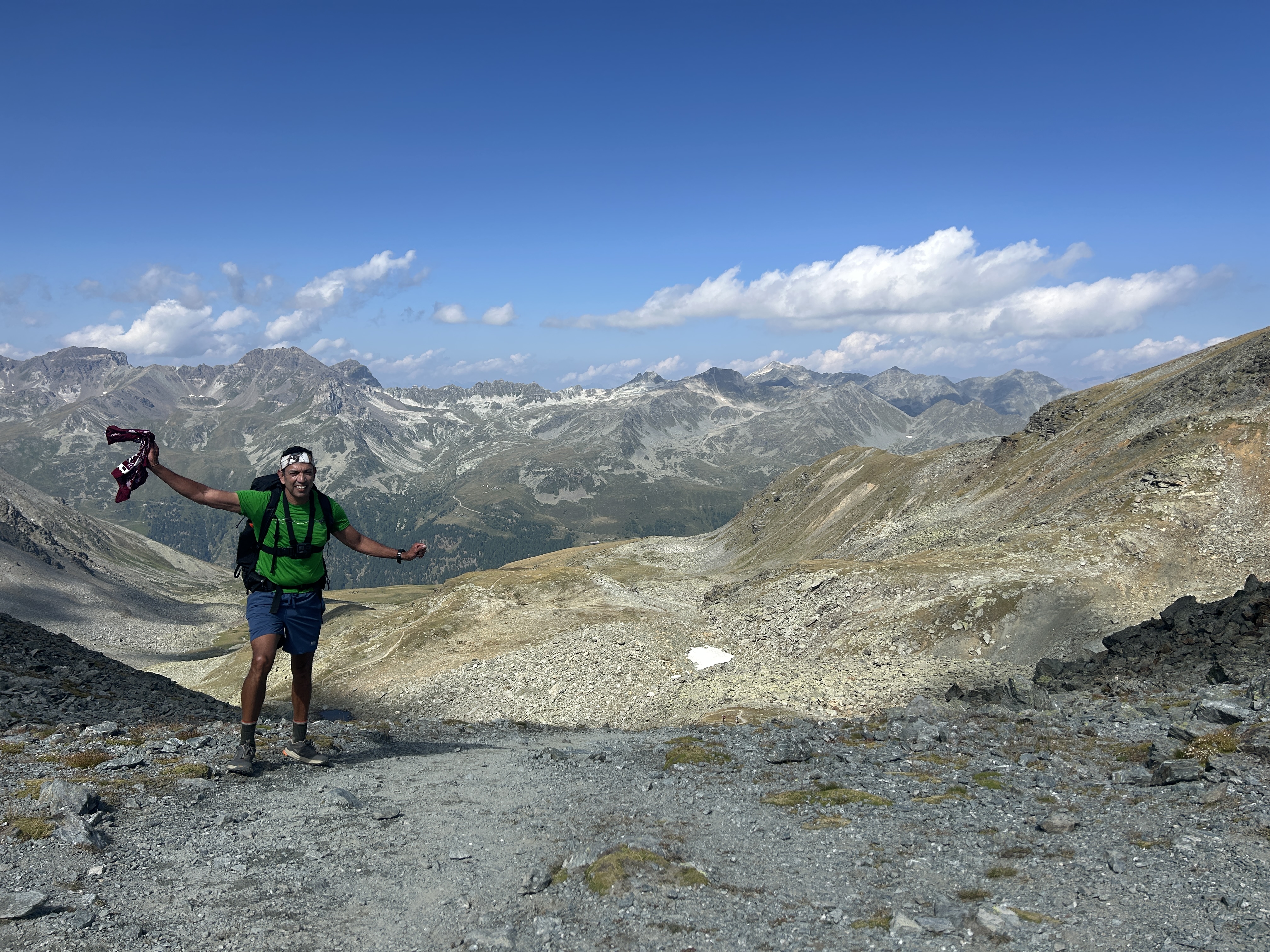 Richard Flores arms wide open at a rocky pass on the Walker's Haute Route, mountain panorama stretching behind him