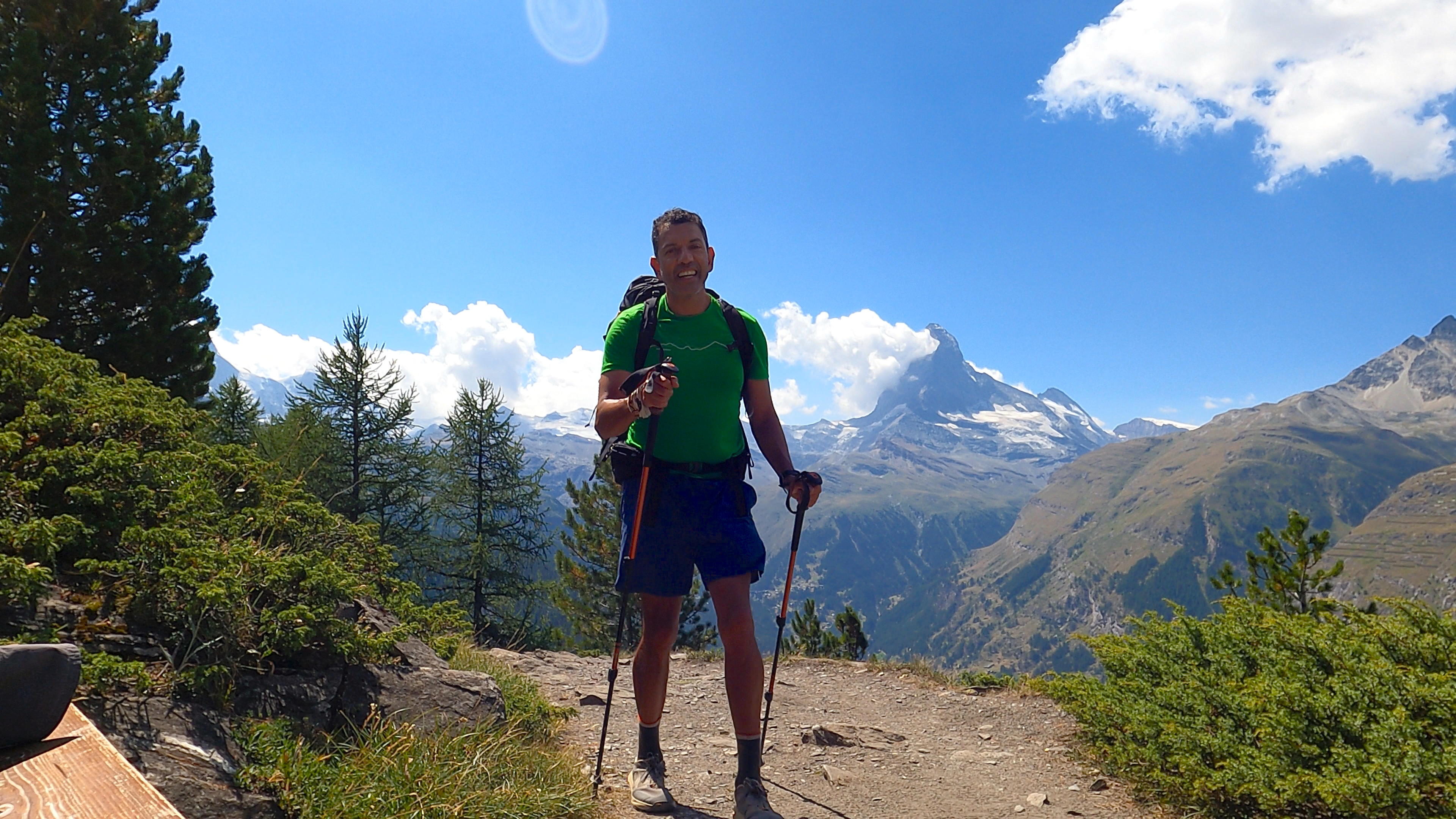 Richard Flores walking through Zermatt with the Matterhorn visible behind him, green shirt, smiling